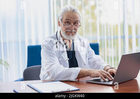 Senior healthcare worker with stethoscope using laptop while working at doctor's office Stock Photo