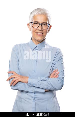 Businesswoman Expert! Beautiful smiling cute senior woman with glasses and a blue shirt with short white hair and glasses posing in front of gray back Stock Photo