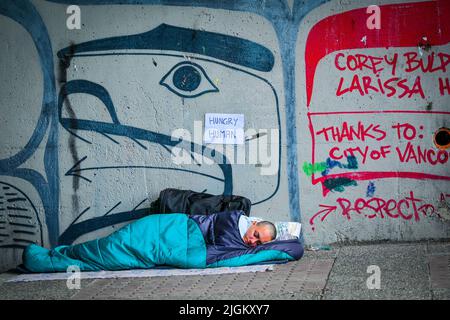 Hungry homeless person sleeping under overpass, Vancouver, British Columbia, Canada Stock Photo