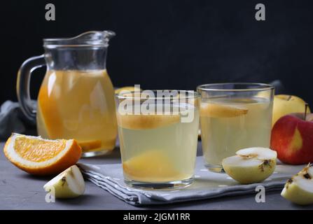 Compote of oranges, apples and lemon in glass and jug on gray background Stock Photo