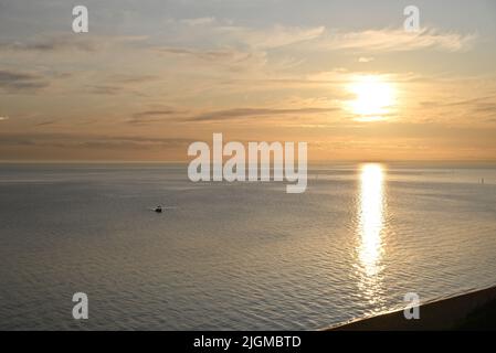 Sun setting over the calm sparkling waters of Port Phillip Bay, with light cloud in the sky, as a small boat heads towards the shore Stock Photo