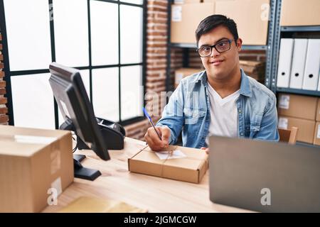 Down syndrome man ecommerce business worker writing on package at office Stock Photo