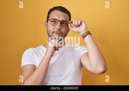Hispanic man holding glasses serious face thinking about question with hand on chin, thoughtful about confusing idea Stock Photo