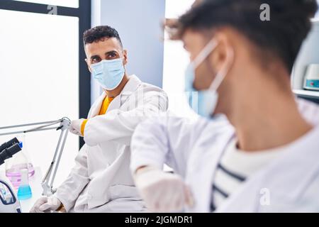 Two man scientists doing elbow greeting at laboratory Stock Photo