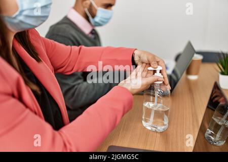 Two hispanic business workers wearing medical mask using sanitizer hands gel at the office. Stock Photo