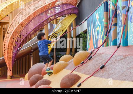 Happy asian boy pulling rope to climbing up on playground at the city park. kid playing outdoor after class at preschool. Stock Photo