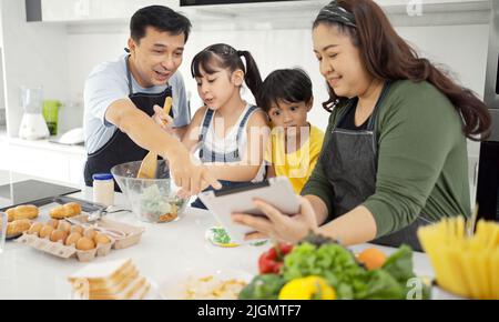 Happy asian parents and their kids having fun while cooking and following recipe on the internet. Stock Photo