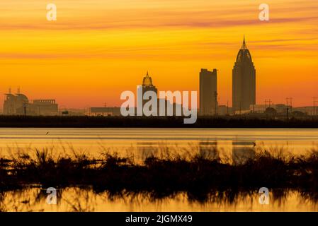 The setting sun paints the sky beyond the skyline of Mobile, Alabama, as seen from across Mobile Bay in a composite image. Stock Photo