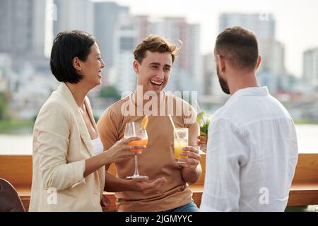 Joyful colleagues chatting and laughing at rooftop party Stock Photo