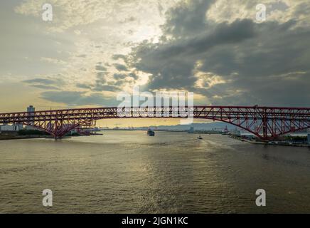 Sun shines through clouds on bridge over river and distant cargo ship Stock Photo