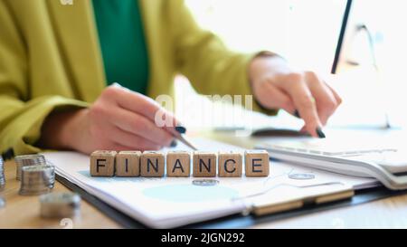 Woman pointing with pen on word finance collected of wooden blocks Stock Photo