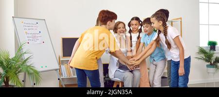 Schoolchildren and their teacher put their hands up one on top of other for support and motivation. Stock Photo