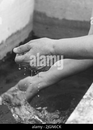 Woman watering and washing on a public foutain in Castell'Arquato Italy.Pure and precious to nature. Shot of hands held out to catch a stream of water Stock Photo