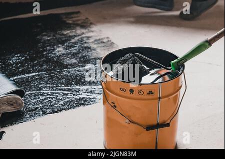 Applying hot resin to the floor for waterproofing, roller and bucket of resin, black and liquid resin. Stock Photo