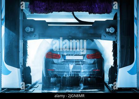 A grey car running through an automatic car wash with brushes and water hitting vehicle. Stock Photo