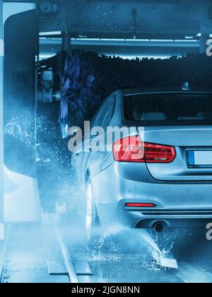 A grey car running through an automatic car wash with brushes and water hitting the vehicle. Stock Photo