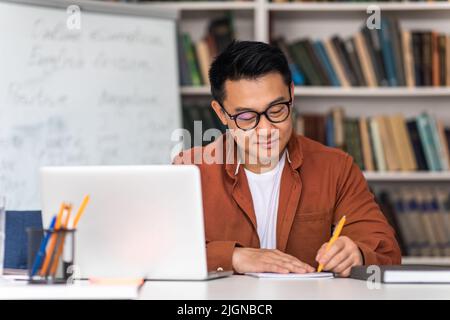 Asian Teacher Writing Using Laptop Having Online Lecture In Classroom Stock Photo