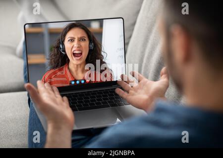 Man Using Laptop, Having Video Call With Angry Female In Headset Stock Photo