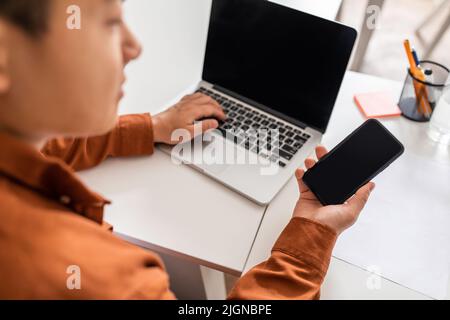 Asian Businessman Using Smartphone And Laptop With Empty Screens Indoor Stock Photo