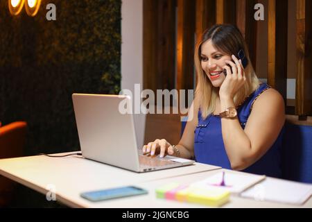 Entrepeneur woman talking on phone smiling with a laptop writing Stock Photo