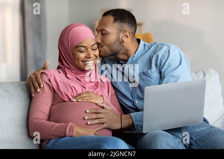 Romantic Islamic Spouses Awaiting Baby Relaxing With Laptop At Home Stock Photo