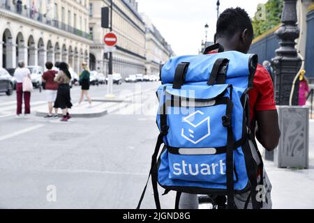 a delivery courier wearing a bright blue Stuart insulated backpack while riding a bicycle on the Rue de Rivoli in Paris, France Stock Photo