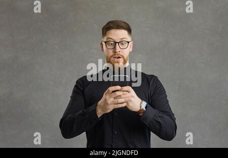 Studio shot portrait impressed excited shocked man looking at smartphone screen Stock Photo