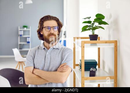 Successful confident Caucasian man wearing glasses with arms crossed stands in modern office Stock Photo