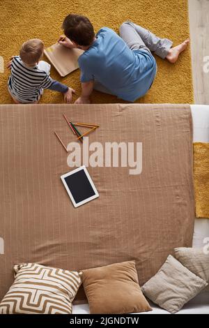 Directly above view of father in pajamas sitting on carpet with son and drawing in sketchbook at home Stock Photo
