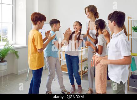 Funny schoolchildren and their positive female teacher play fun games in creative lesson. Stock Photo