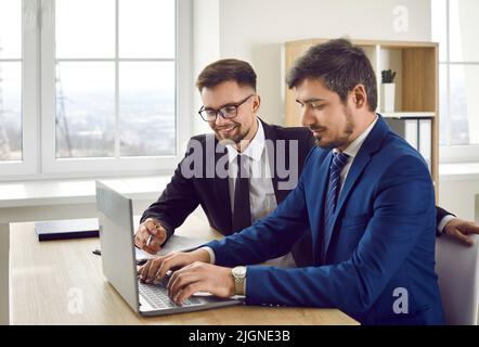 Young positive Caucasian man working with laptop creating presentation sits at office desk Stock Photo