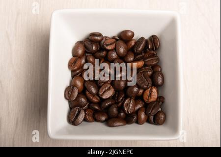 Coffee beans in a square white dish on a white wood background shot from above Stock Photo