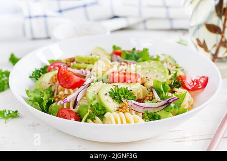 Fusilli pasta salad with avocado, tomatoes, fresh green lettuce, red onion and mustard dressing on white background. Vegetarian healthy lunch. Stock Photo