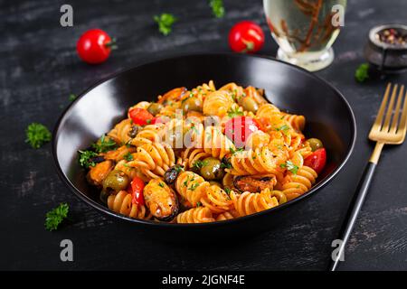 Classic italian pasta fusilli marinara with mussels, green olives and capers on dark table.  Fusilli pasta with sauce marinara Stock Photo