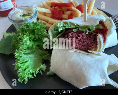 Not a sandwich but a wrapped, a pastrami with the thin slices of beef in a thick layer garnish with fresh salad and secret sauce and crispy fries. Stock Photo