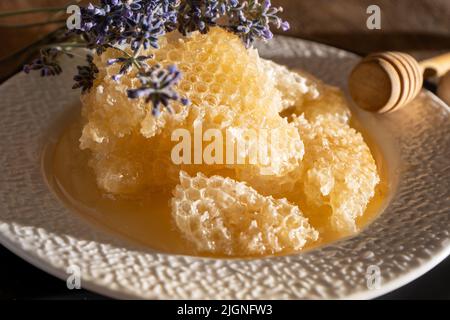 Honey and honeycombs on a white plate. Sweet food in a bowl on the table. A product of beekeeping. Lavender flower. Stock Photo