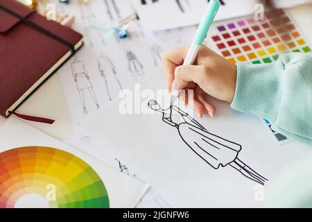 Close-up of unrecognizable female designer sitting at table with color palettes and sketches and creating design of dress Stock Photo
