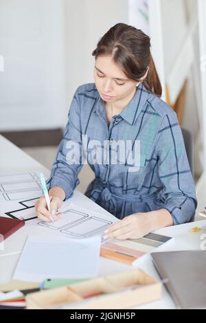 Serious beautiful girl concentrated on ui design sitting at desk and creating interface for gadgets Stock Photo