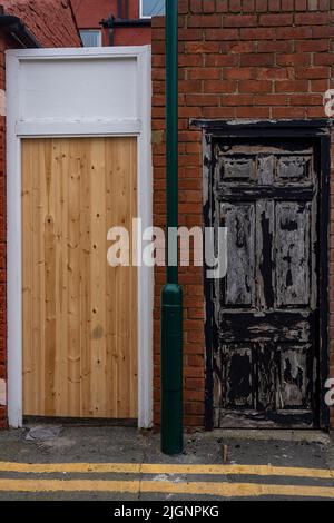 two wooden doors, one new, one old, with lamp post between and two yellow lines in front Stock Photo