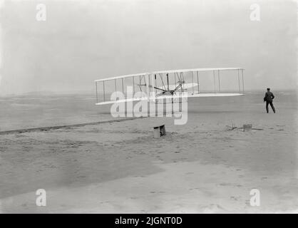 Vintage photo dated December 17th 1903 of the Wright Flyer on its first powered and controlled flight by Orville Wright with his brother Wilbur Wright at the side of the machine.  The first flight took place at Kitty Hawk, North Carolina, USA Stock Photo