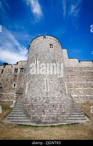 A dramatic low-angle view of Windsor Castle's stone curtain wall and round tower against a blue sky with wispy clouds, Berkshire, England. Stock Photo