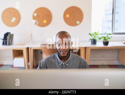 A Black businessman works at his wide screen computer in the office Stock Photo