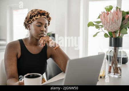 Black African woman working from home, looking at laptop. Laptop and smartphone on home office table Stock Photo