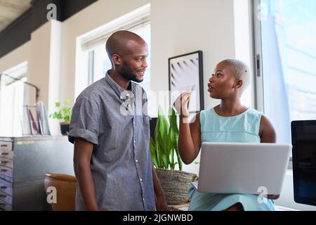 A Black woman explains something to her male colleague in trendy office Stock Photo