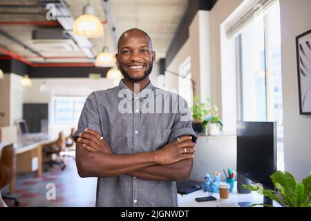 An attractive Black man stands with arms crossed in creative office workplace Stock Photo