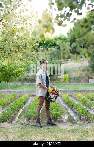 Vertical side view of young handsome man with a basket full of vegetables and the garden orchard in the background Stock Photo
