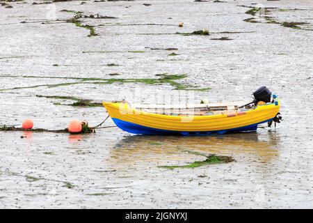 Small yellow and blue rowing boat with outboard motor resting on mud at low tide Stock Photo