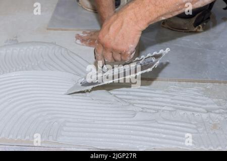 Putting adhesive on the bathroom floor by spreading wet mortar before applying tiles Stock Photo