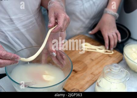 The process of making cheese with a pigtail. Hands kneading cheese in milk. Stock Photo