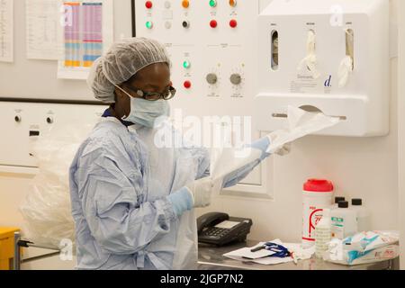 An NHS nurse in scrubs checks a patients records in an operating theatre during an operation. Stock Photo